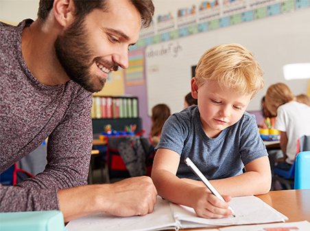 Elementary School Teacher Giving Male Pupil One To One Support In Classroom
